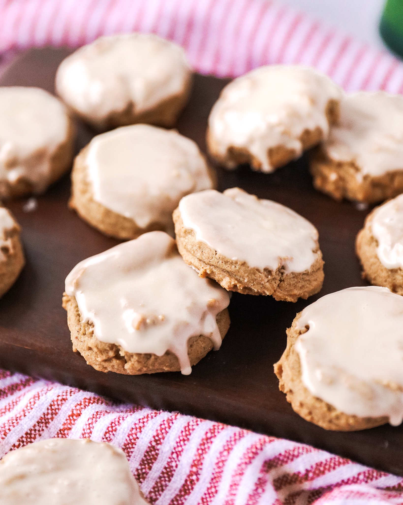 10 iced gingerbread cookies sit on a dark brown wooden cutting board, with a striped red and white towel underneath.